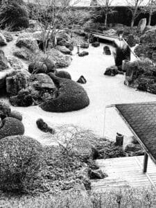 Japanischer Garten in Schwarz-Weiß mit Felsen, Bäumen und sorgfältig geharktem Sand.