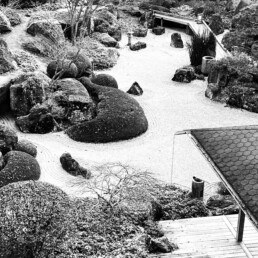 Japanischer Garten in Schwarz-Weiß mit Felsen, Bäumen und sorgfältig geharktem Sand.
